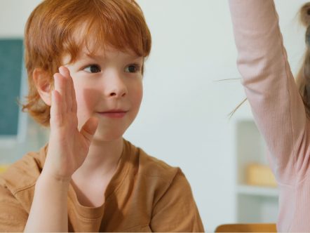 Rudowłosy chłopiec podnoszący rękę na lekcji