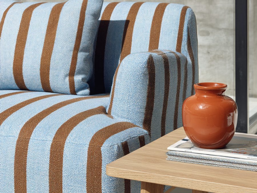 Fotel w niebiesko-brązowe pasy i ceramiczny wazon na stoliku